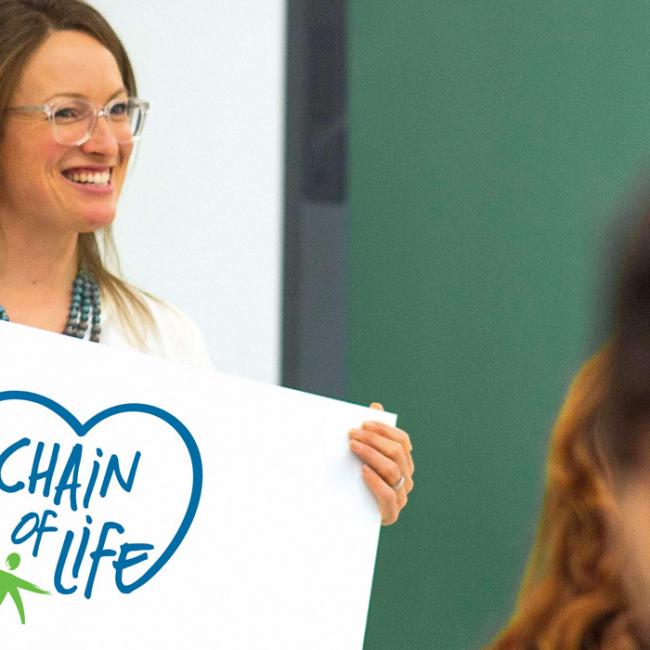 Teacher holding sign with Chain of Life logo
